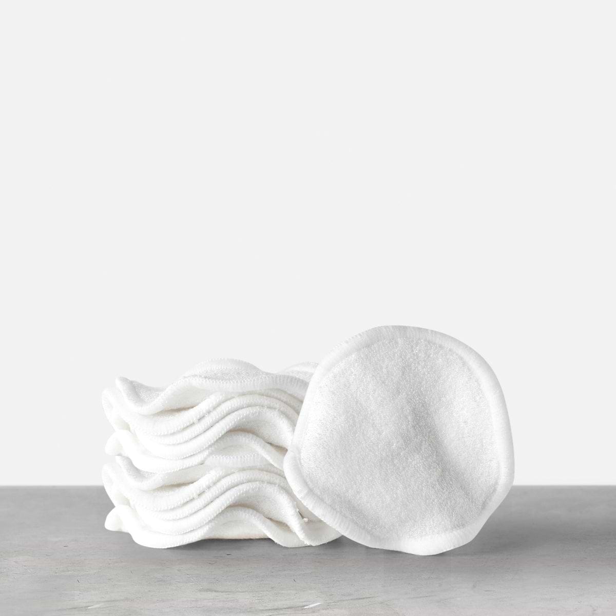 A stack of Medik8 reusable bamboo cotton pads displayed on a grey surface. One pad stands upright, showcasing its soft, textured fabric.
